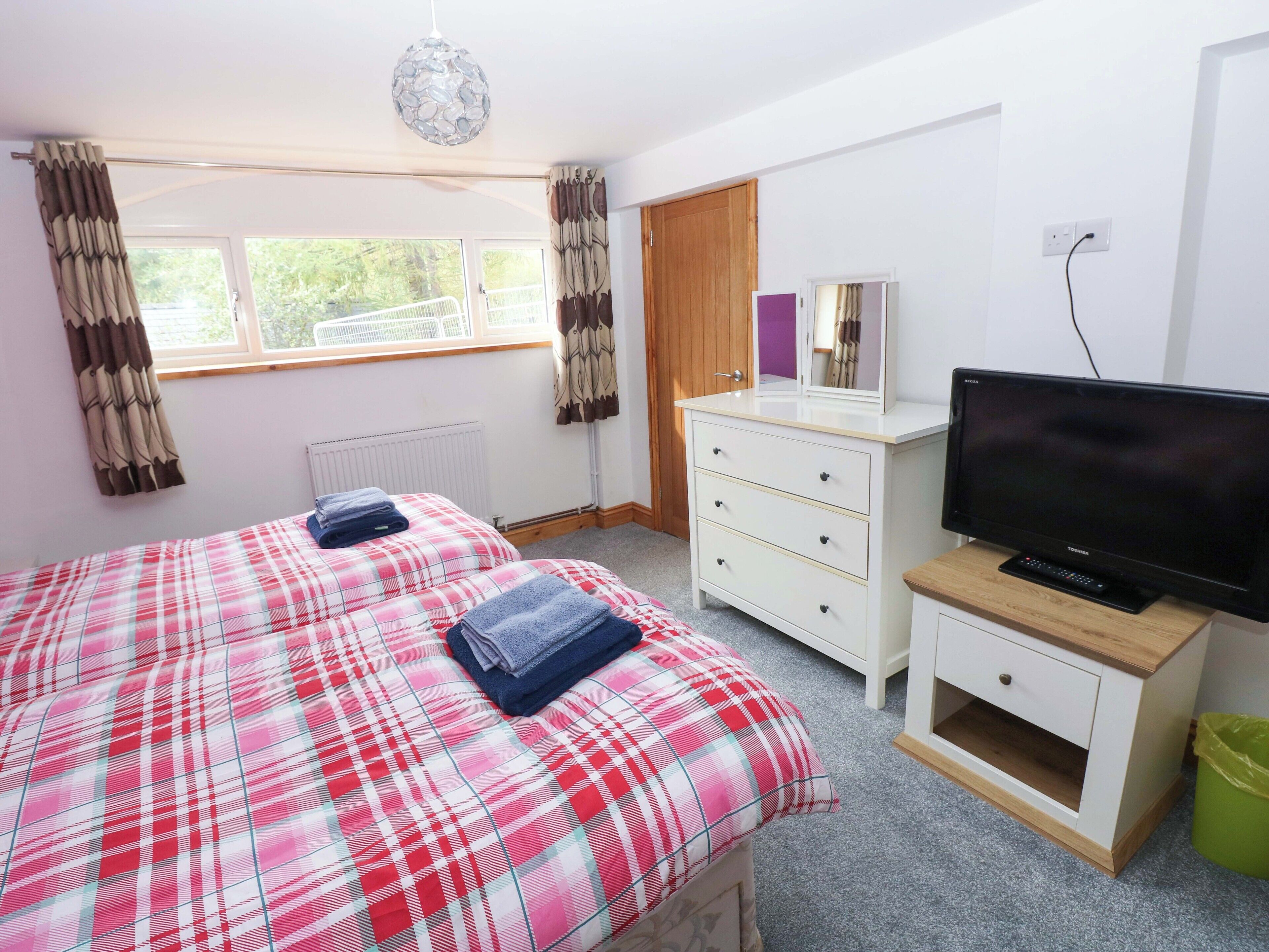 Ein Schlafzimmer mit Bett, Kommode, Fernseher und einem Fenster mit Vorhängen.