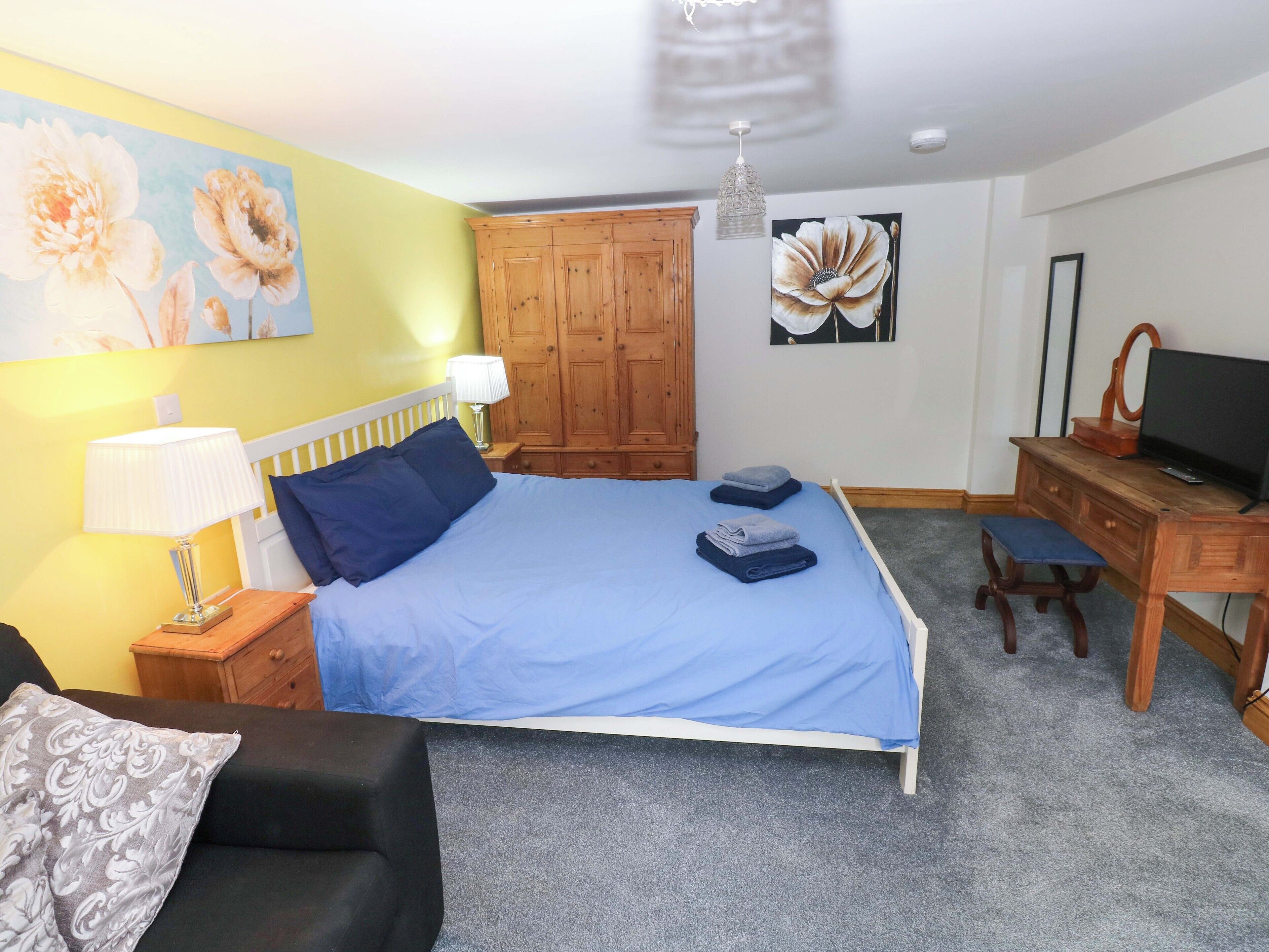 A bedroom with a bed, a desk, a chair, a TV, and artwork on the walls.