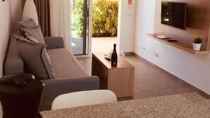 A modern living room with a sofa, a coffee table, a TV mounted on the wall, and a view of the outdoors. - Alsol Los Leones bungalows - Adults Only (San Bartolomé de Tirajana)