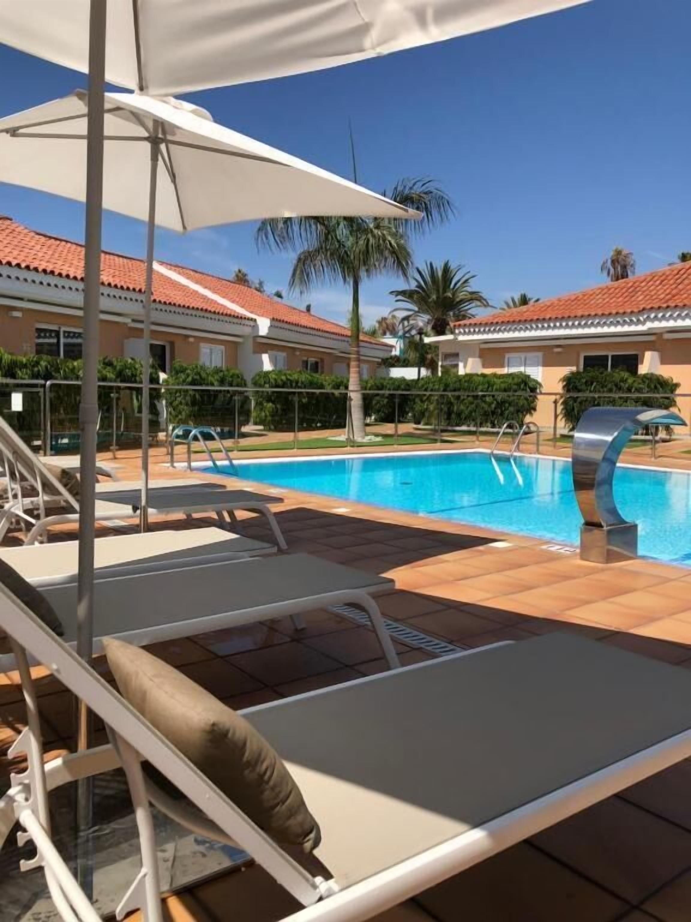 A poolside area with lounge chairs, a pool, and a building with a tiled roof.