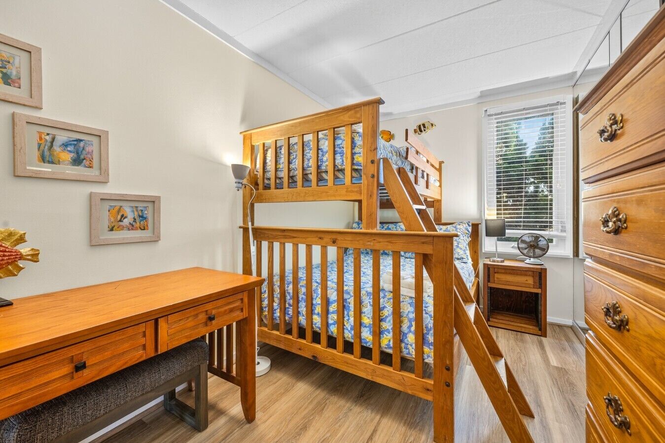 A room with a bunk bed, wooden dresser, desk, and artwork on the wall.