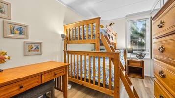 A room with a bunk bed, wooden dresser, desk, and artwork on the wall.