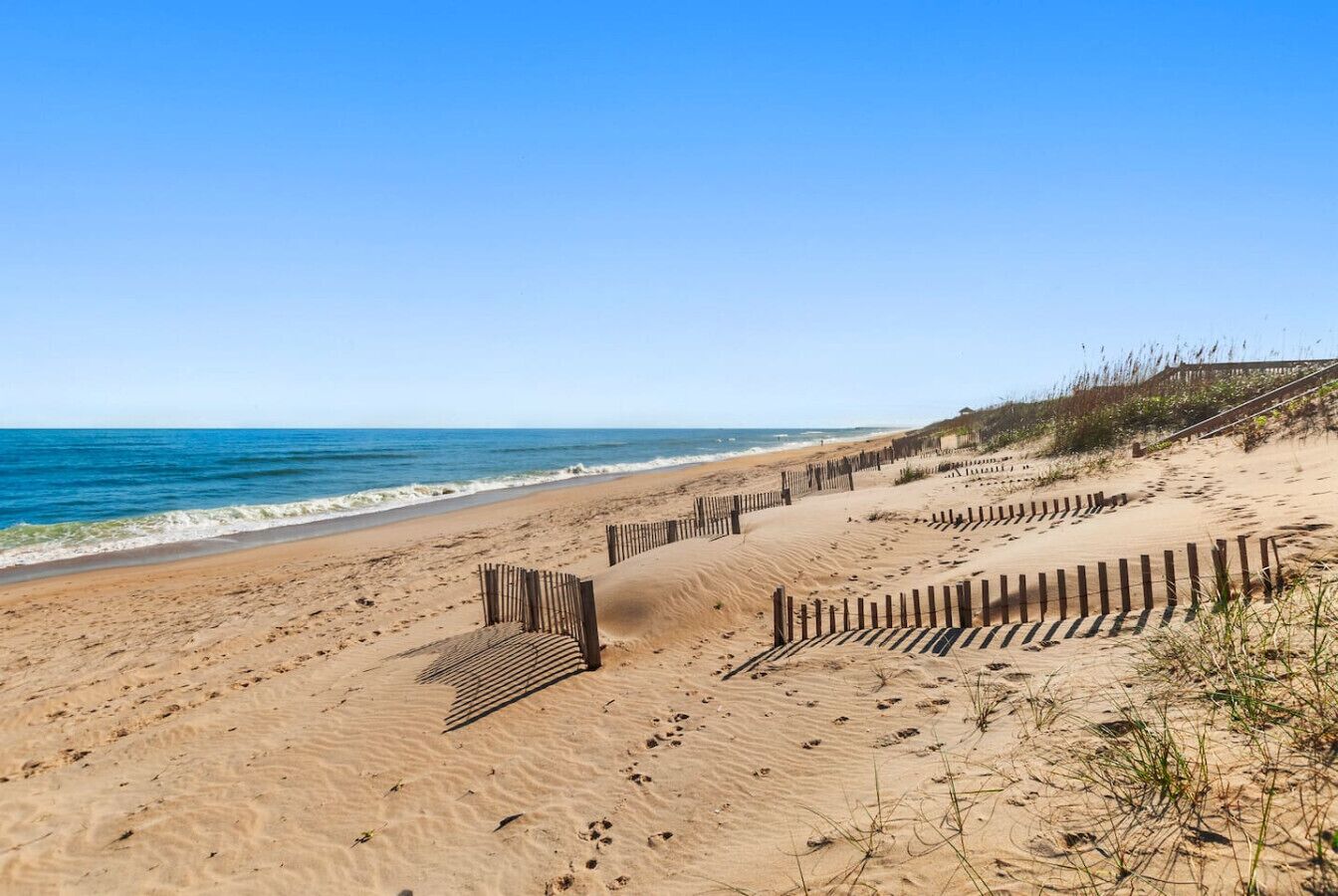 A sandy beach with wooden groynes and a clear blue sky.