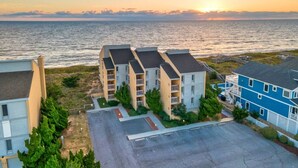 A coastal residential area with a row of townhouses, a parking lot, and a view of the sea at sunset. - Direct Ocean Front 2BR w/ Pool (Nags Head)