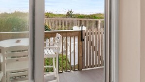 A balcony with a white chair and table, a wooden fence, and a view of the beach. - Direct Ocean Front 2BR w/ Pool (Nags Head)