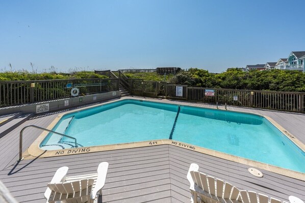 A rectangular swimming pool with a wooden deck, surrounded by a fence and a lifeguard stand.