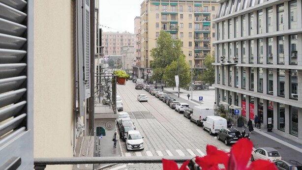 Vista de la calle desde un balcón, con una fila de coches aparcados, una línea de tranvía y edificios al fondo.