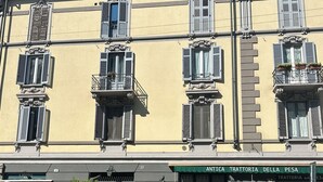 Un edificio con varias ventanas, algunas con contraventanas, y un escaparate con un letrero.