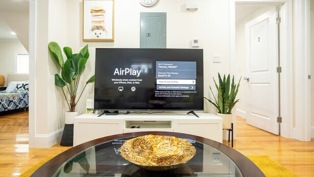 Ein Wohnzimmer mit Flachbildfernseher auf einem Schrank, einem gerahmten Bild an der Wand und einer Topfpflanze.