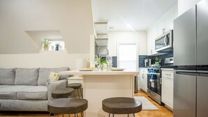 Eine moderne Küche mit Kochinsel, Barhocker, einem grauen Sofa und einem Essbereich mit einem kleinen Tisch und Stühlen.
