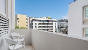 A balcony with white chairs, a view of multi-story buildings, and a clear blue sky.