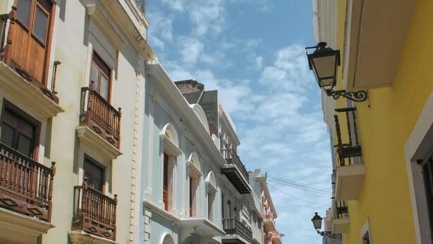 A narrow street with buildings featuring balconies and a street lamp.