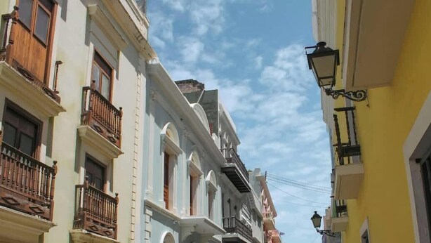 A narrow street with buildings featuring balconies and a street lamp.