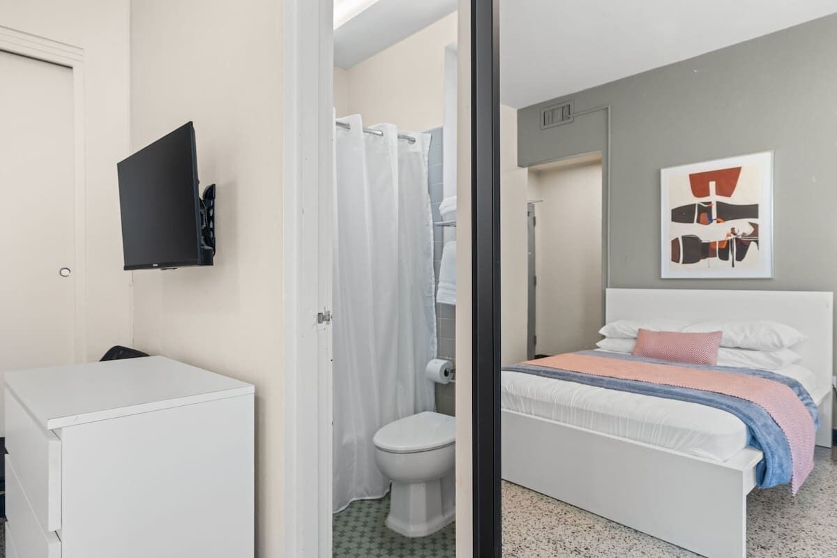 Ein modernes Schlafzimmer mit Bett, Wand-Fernseher, Dusche und Toilette.