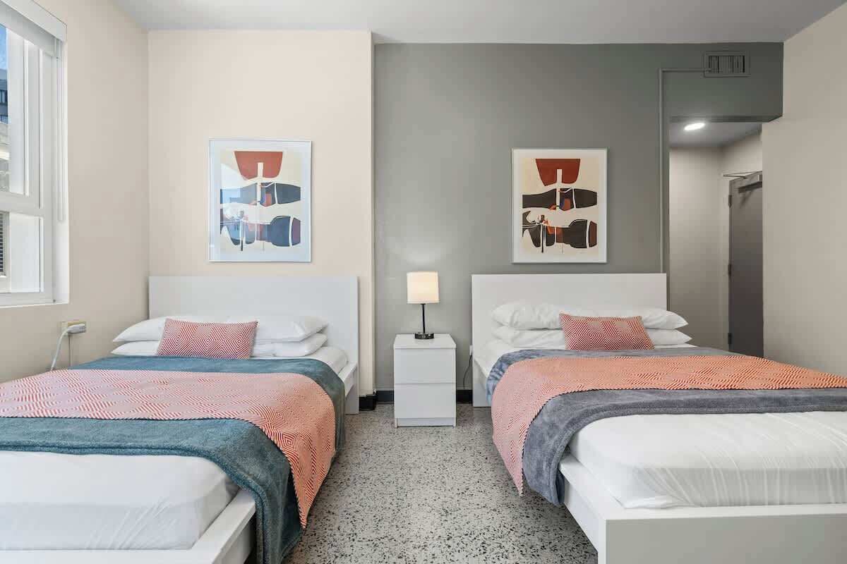A hotel room with two beds, a nightstand, and artwork on the walls.
