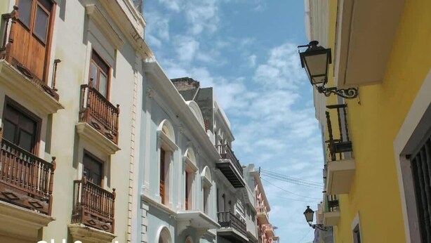 A narrow street with buildings featuring balconies and a street lamp.