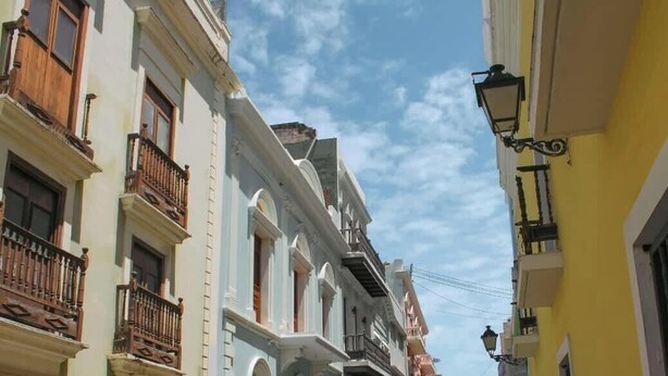 A narrow street with buildings featuring balconies and a street lamp.