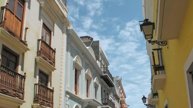 A narrow street with buildings featuring balconies and a street lamp.