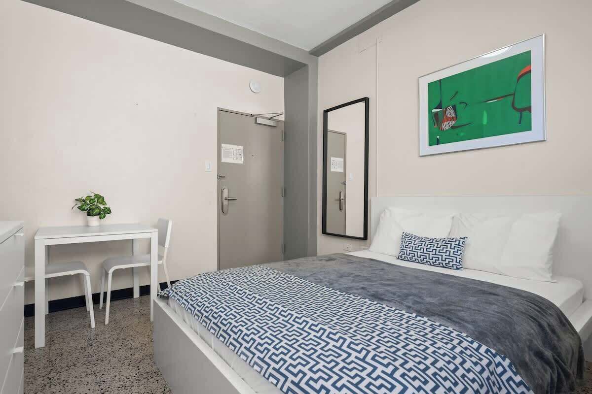 Un dormitorio con cama, escritorio y sillas, un espejo y un cuadro en la pared.