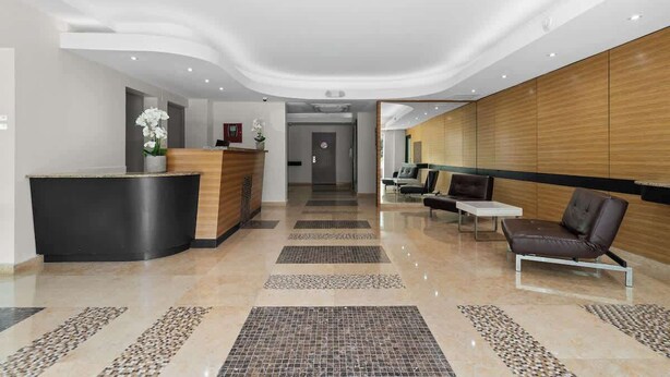 A modern hotel lobby with a reception desk, seating area, and a hallway leading to other rooms.
