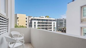 A balcony with white chairs, a view of multi-story buildings, and a clear blue sky. - With Balcony | King Bed |  Free Parking | AC (San Juan)