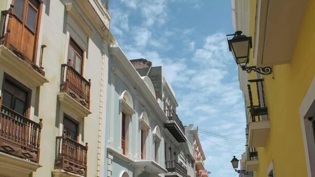 A narrow street with buildings featuring balconies and a street lamp.