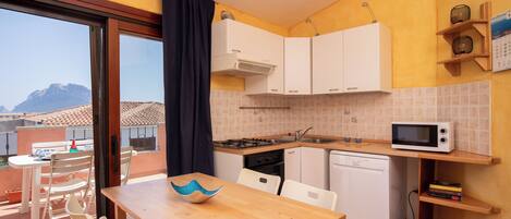 Una cocina compacta con armarios blancos, un microondas y un comedor con mesa y sillas de madera.