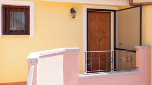 A yellow building with a wooden door, a window with metal bars, and a metal railing.