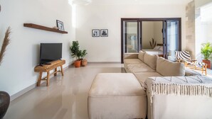 Un salon moderne avec un téléviseur à écran plat, un canapé et une table basse. On y trouve une étagère en bois avec des photos et une plante en pot.