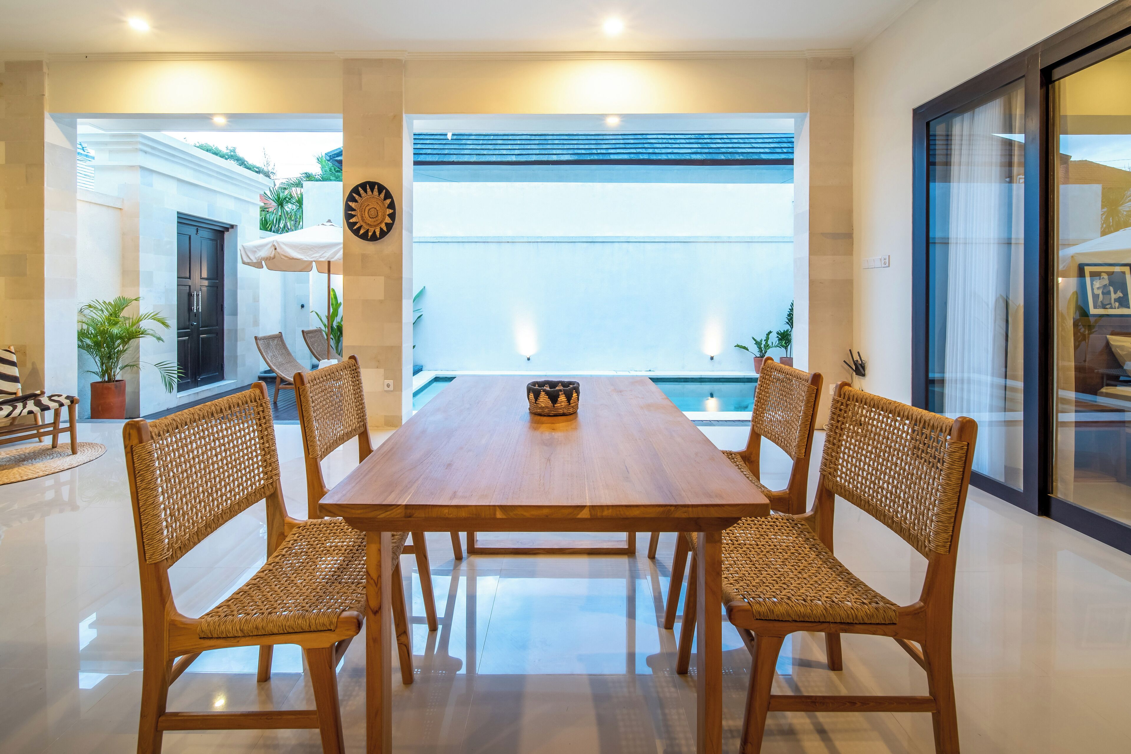 A spacious dining area with a wooden table and woven chairs, a large window with a view, and a decorative wall piece.