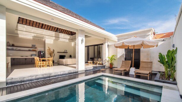 Un espace piscine extérieur moderne, doté d’un coin salon couvert, de chaises longues et d’un espace aménagé pour les repas.