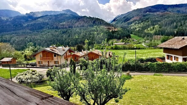 Ein ländliches Dorf mit traditionellen Holzhäusern, umgeben von üppigen grünen Feldern und Bergen im Hintergrund.