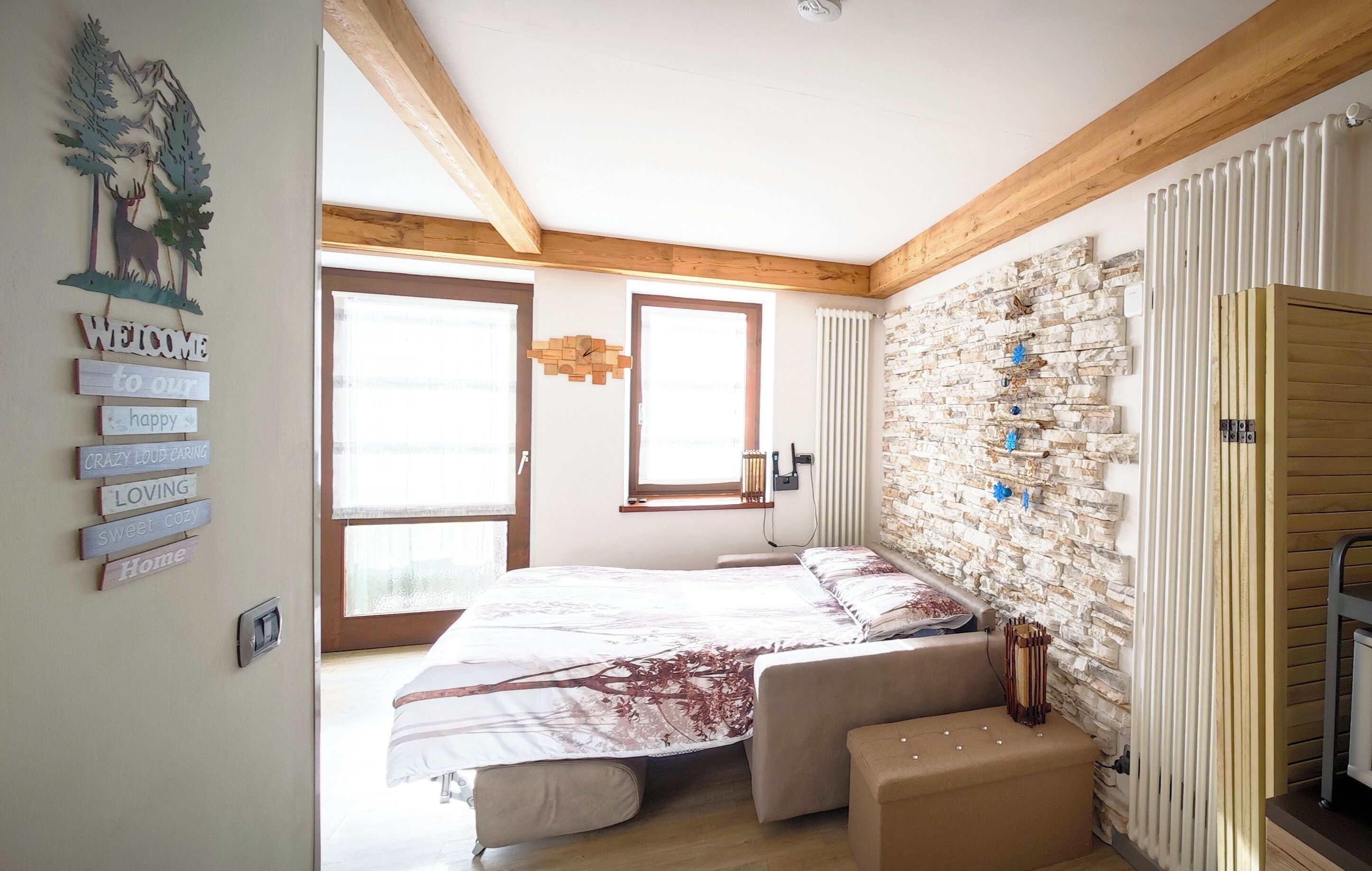 Une chambre avec un lit, un mur en pierre, des poutres en bois et une pancarte de bienvenue.