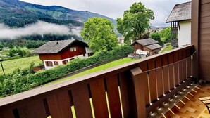 Ein Balkon mit Holzboden, mit Blick auf ein Dorf mit Häusern und einem Berg im Hintergrund.
