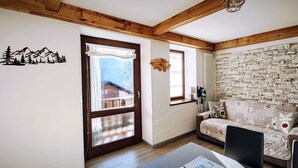 Ein gemütliches Wohnzimmer mit Steinwand, Holzbalkendecke und einer Couch mit Rentierkissen.