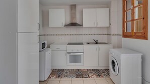 Una cocina compacta con armarios blancos, microondas, horno, lavabo y lavadora.