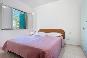 Une chambre à coucher avec un lit, une fenêtre avec des volets, une lampe de chevet et une commode.