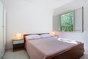 A bedroom with a bed, two bedside tables with lamps, a nightstand, a window, and a door.