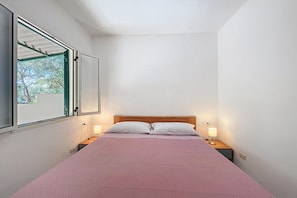 Una cama individual con cabecera de madera, dos lámparas de noche y una ventana con vista a árboles.