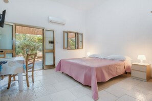A bedroom with a bed, bedside tables, a chair, a table, and a sliding glass door leading to an outdoor area. - Studio 'Sabbia D'oro' with Shared Pool and Wi-Fi (Scialara)