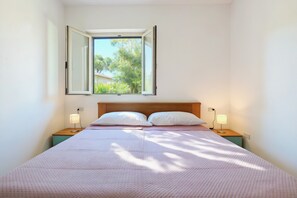 A bedroom with a bed, two bedside tables, a window, and a view of trees.