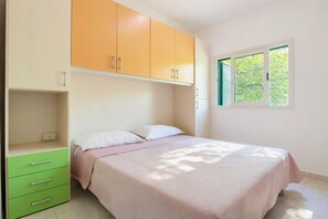 Une chambre à coucher avec un lit, une commode verte et une fenêtre donnant sur des arbres.