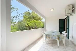 Ein Balkon mit Tisch und Stühlen, Blick auf Bäume und eine Klimaanlage.