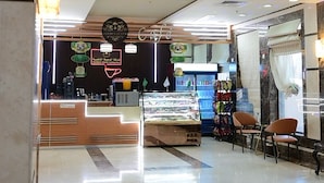 A cafe with a modern interior, a counter with a display case, and a seating area with chairs. - Wefaq Al-Mashaer Hotel (Makkah)