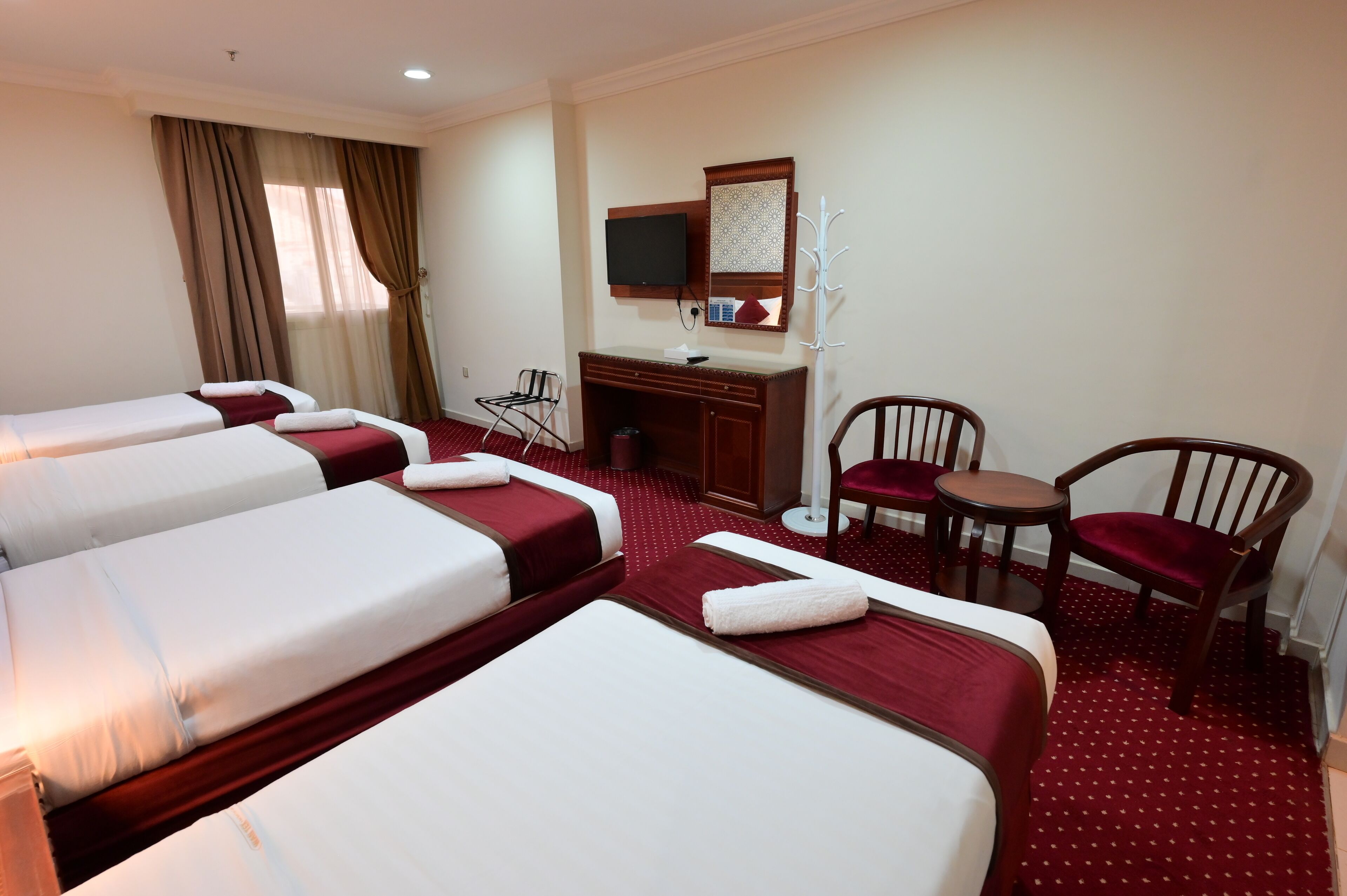 A hotel room with three beds, a desk, a chair, a TV, and a coat rack.