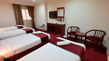 A hotel room with three beds, a desk, a chair, a TV, and a coat rack.