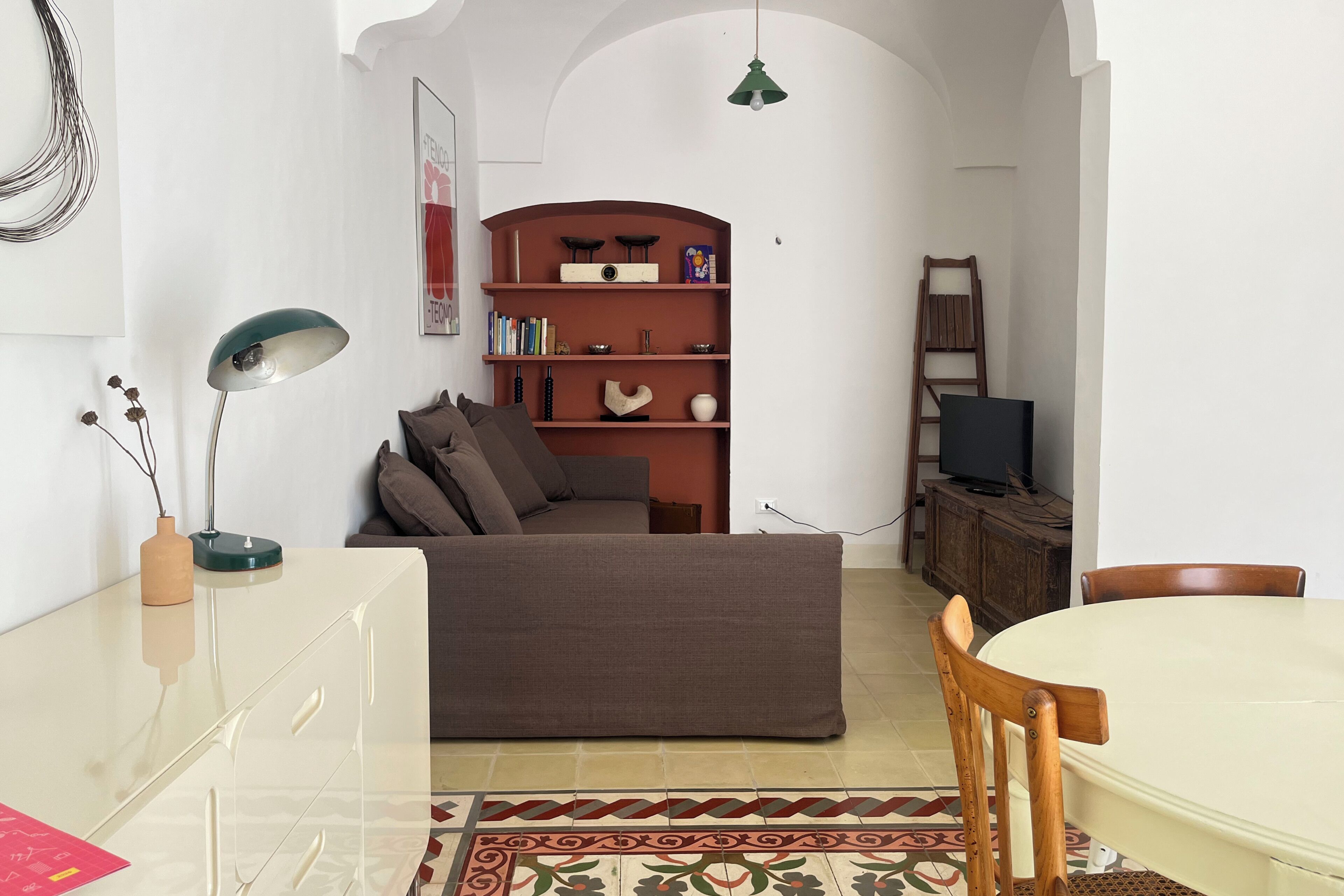 A living room with a sofa, a television, a bookshelf, and a dining area with a table and chairs.