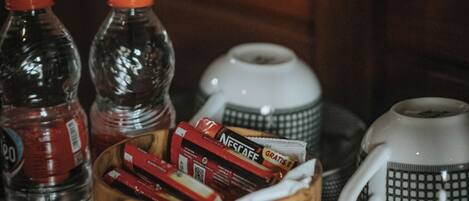 A wooden tray with two bottles, a wooden bowl with snacks, and two coffee cups.