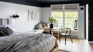 Une chambre à coucher comprenant un lit, une table ronde, une chaise, une plante en pot et une fenêtre donnant sur un paysage verdoyant.