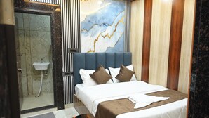 A modern hotel room with a large bed, a bathroom with a glass shower enclosure, and a marble wall. - Hotel Kumar Continental (Jhusi)